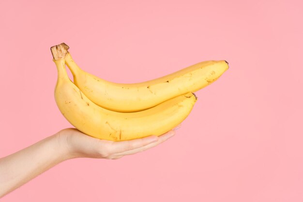 Bananes jaunes dans la main d'une femme sur fond rose
