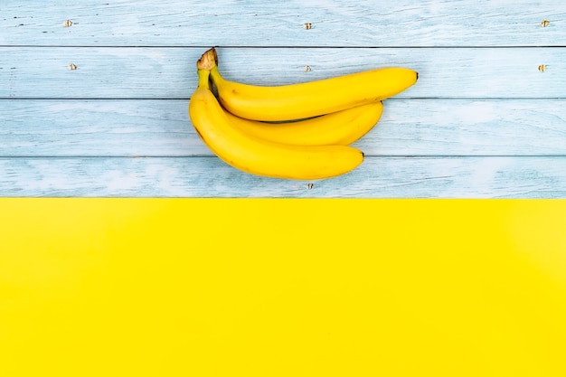 Les bananes jaunes se trouvent sur un fond en bois bleu et un fond jaune.
