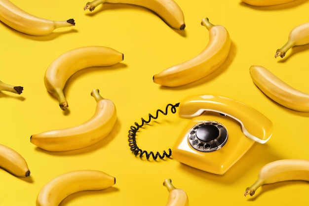 Des bananes à motif créatif et un vieux téléphone jaune avec un motif d'ombres dures sur un fond plat jaune