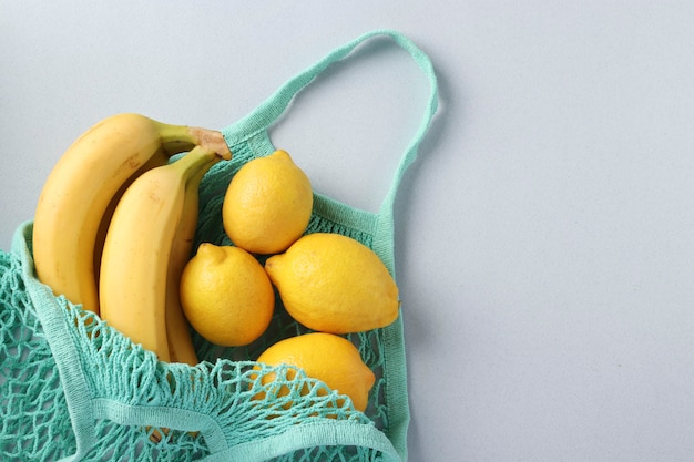 Bananes mûres jaunes et citrons dans un sac en filet turquoise sur une surface légère, concept zéro déchet, espace pour le texte