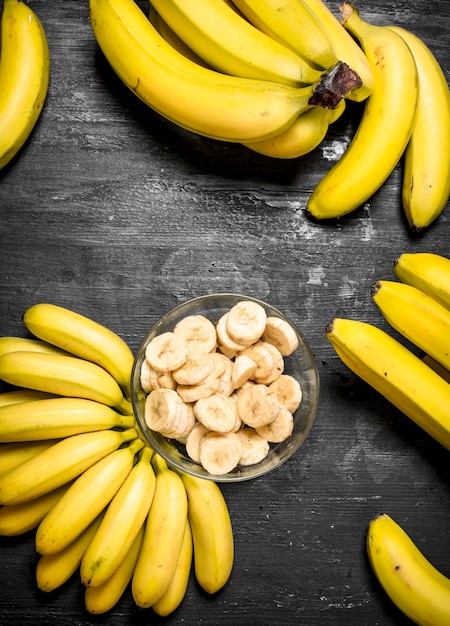 Bananes mûres avec des morceaux de bananes tranchées dans un bol. Sur un tableau noir.