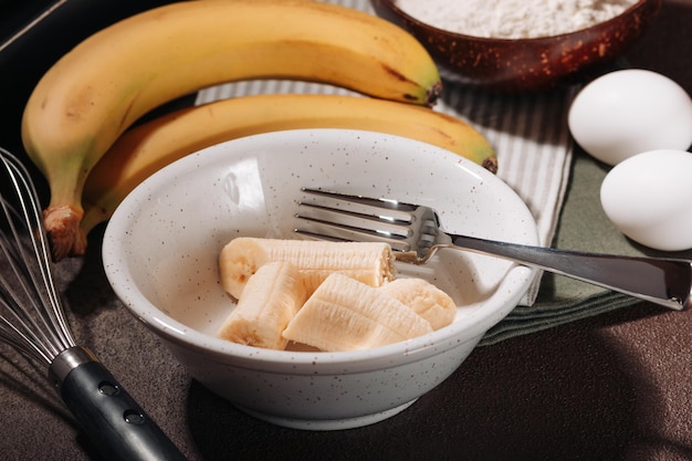 Bananes pelées et cassées dans un bol en céramique - ingrédient pour la cuisson du pain aux bananes sur fond marron