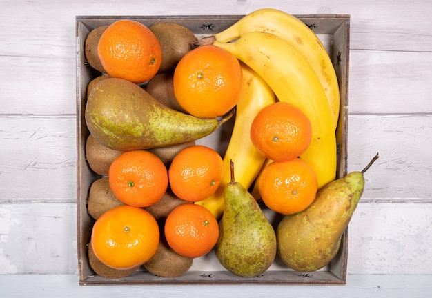 Bananes, poires de conférence, mandarines et kiwis placés dans un vieux plateau en bois sur une surface de vieux plancher en bois