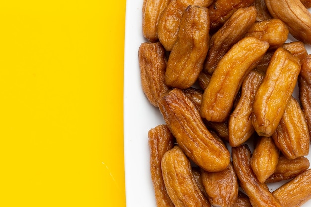 Bananes séchées au soleil en plaque blanche sur fond jaune.