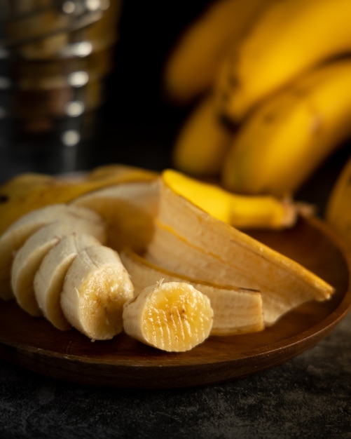 Bananes servies sur table avec fond noir et assiette en bois