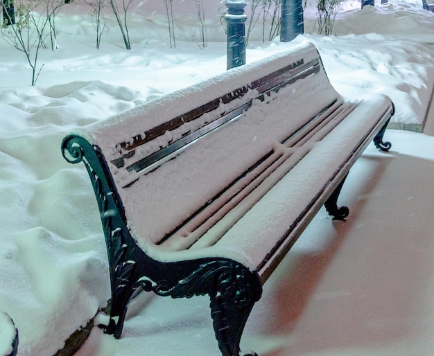 Un banc sous la neige la nuit dans le parc.