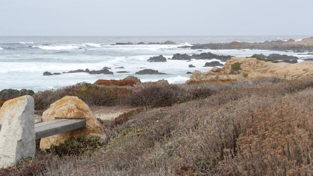 Banc vide en bois de la côte de l'océan rocheux escarpé Monterey en Californie