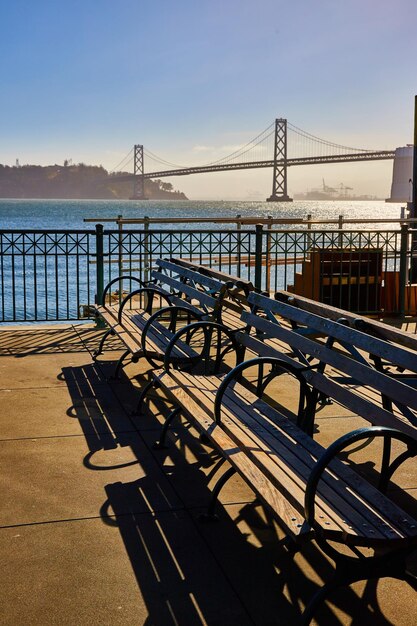 Photo des bancs sur le quai avec des ombres sombres sinistres un jour d'été brillant avec le pont de la baie d'oakland