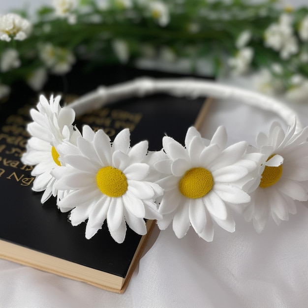 Un bandeau de fleurs blanches avec un centre jaune se trouve à côté d'un livre noir.