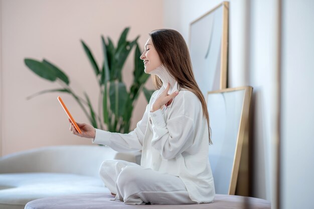 Bandes sur le cou. Jeune femme en blanc assis sur une chaise douce et faire une photo de bandes sur son cou