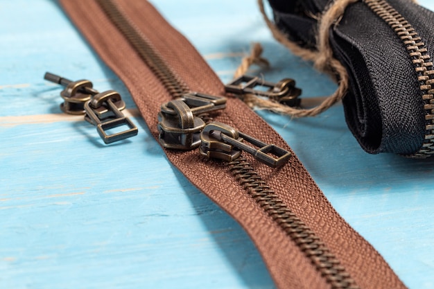 Bandes de fermetures à glissière en laiton en métal noir et marron avec des curseurs pour la main sur le fond en bois bleu