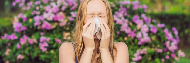 BANNIÈRE Concept d'allergie au pollen. La jeune femme va éternuer. Arbres en fleurs au format long d'arrière-plan