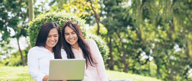 Bannière Asiatique deux femmes parlant à l'aide d'un ordinateur portable s'asseoir sur un pré vert au parc verdoyant Panorama Amitié filles discuter parler regarder ordinateur portable petite entreprise Belles femmes rire parler ensemble avec espace copie