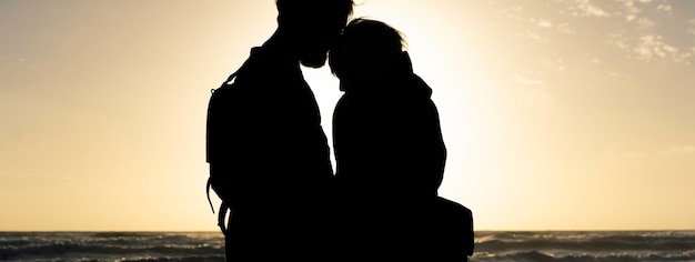 Bannière horizontale avec la silhouette d'un jeune hipster voyageant en couple portant un sac à dos vintage debout au magnifique coucher de soleil sur une plage sauvage Concept d'amour et culture des jeunes