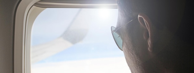 Bannière horizontale ou en-tête avec un jeune passager regardant par la fenêtre de l'avion en vol Vue latérale d'un bel homme contre la fenêtre de l'avion assis et regardant Voyageur solitaire