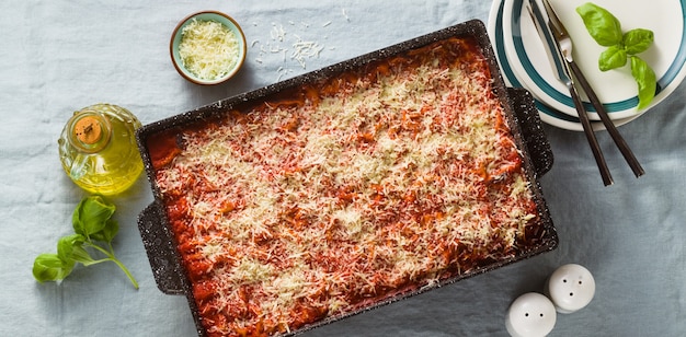 Bannière de lasagne végétalienne aux lentilles et petits pois dans une plaque à pâtisserie sur une table avec une nappe en lin bleu.