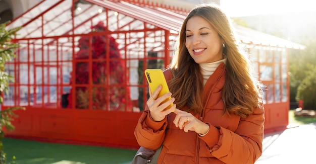 Bannière Panoramique D'une Belle Femme Souriante En Doudoune Tenant Un Smartphone Pendant La Période De Noël