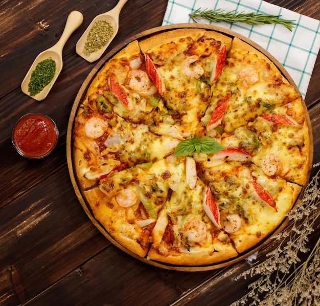 Bannière de pizza aux fruits de mer maison avec crevettes, bâtonnets de crabe, garniture de poivrons sur plateau en bois, table, décorée de sauce tomate, ketchup, ingrédients d'origan avec serviette dans la cuisine et espace de copie.