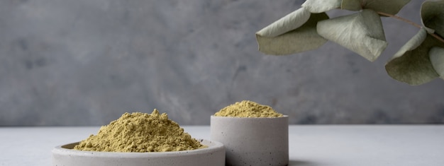 Photo bannière. poudre de henné pour teindre les cheveux et les sourcils et dessiner le mehendi sur les mains sur un socle en ciment gris avec des fleurs séchées ou une fleur blanche.