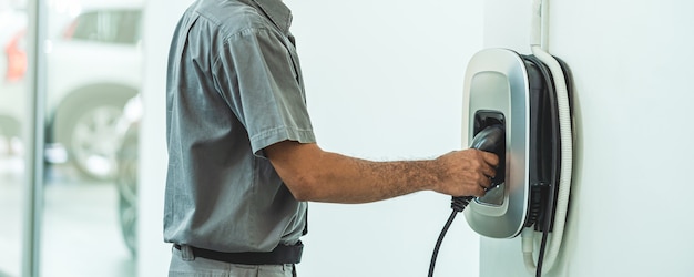 Bannière et scène de couverture de la main Gros plan charger la voiture electrict dans le centre de service de maintenance qui fait partie de la salle d'exposition, de l'économie et de la technologie pour la sécurité du monde concept