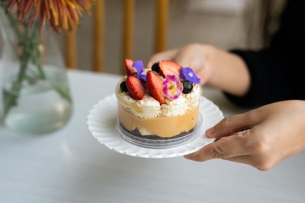 Une Banoffee Pie est servie dans un gobelet en plastique, orné de fleurs et de fraises comme décoration.