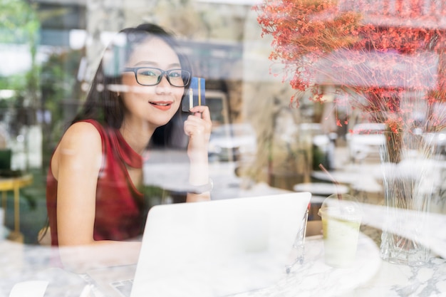 Banque En Ligne Et Concepts De Paiement, Jeune Femme Asiatique Assise Souriant Tenant Une Carte De Crédit En Mains Lors De Vos Achats En Ligne Sur Un Ordinateur Portable Dans Un Café