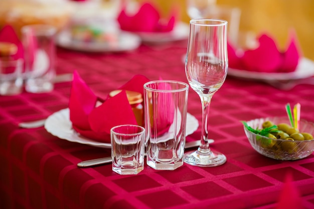 Photo banquet avec table rouge nappe rouge vaisselle blanche couverts en argent et verres à pied à carreaux rouges plus quelques décorations