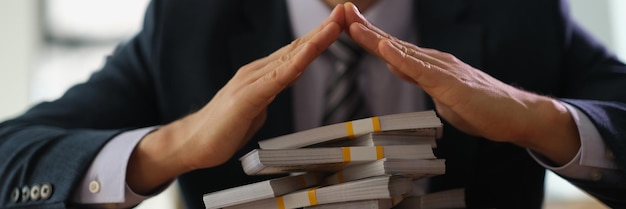 Banquier faisant le toit avec les mains sur des liasses de billets en dollars gros plan