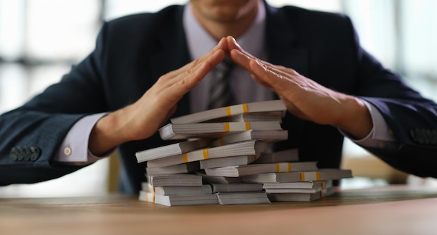 Un banquier fait un toit sur des piles d'argent avec ses mains en gros plan.