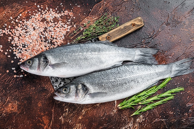 Bar ou bar poisson cru frais sur un couperet avec du sel et des herbes. fond sombre. Vue de dessus.