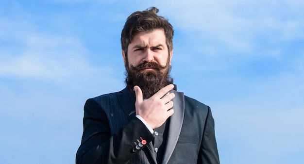 Barbe longue de style vintage Soins de la barbe et de la moustache Poils du visage Tendance de la mode de la barbe Investir dans une apparence élégante Grandir rapidement une barbe épaisse Homme barbu hipster porter costume formel fond de ciel bleu