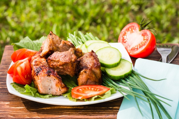 Barbecue sur une assiette avec des légumes sur une table en bois sur le fond d'herbe