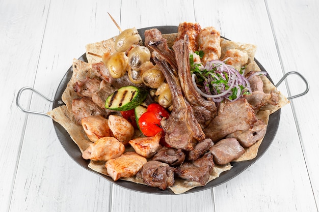 Barbecue assorti de viande, poisson et légumes sur un bol en métal sur une table en bois blanc