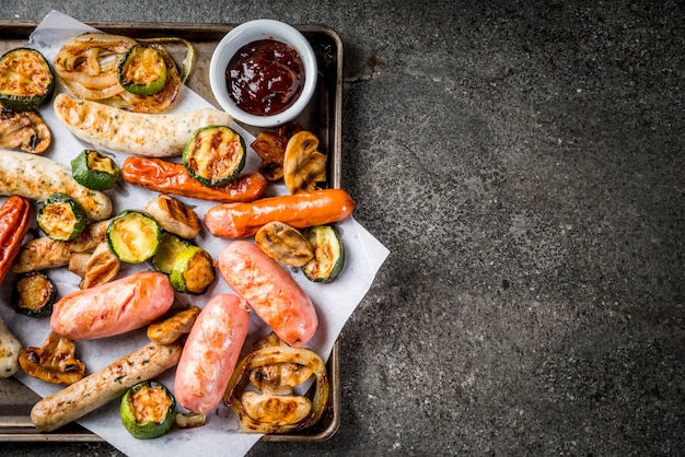 Barbecue. Assortiment de diverses saucisses de viande grillées, avec légumes BBQ champignons, tomates, courgettes, oignons. Sur une table en pierre noire, sur une plaque à pâtisserie, avec sauce. vue de dessus du fond