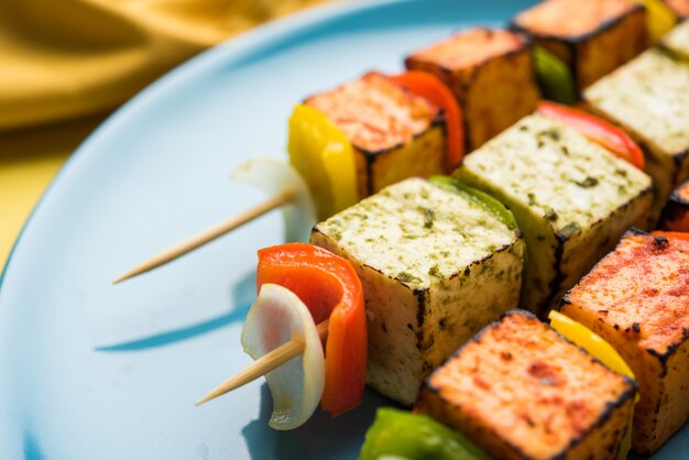 Photo barbecue paneer tikka kabab - cubes de fromage cottage indien tandoori en sauce rouge et blanche en bâtonnets, servis dans une assiette avec chutney vert sur une table colorée ou en bois, mise au point sélective