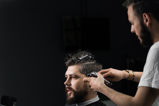 Barber faisant la coiffure pour hipster barbu confiant. Publicité pour salon de coiffure et salon de beauté pour hommes.