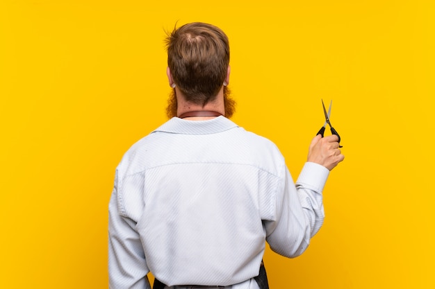 Barber avec une longue barbe dans un tablier sur jaune isolé en position arrière