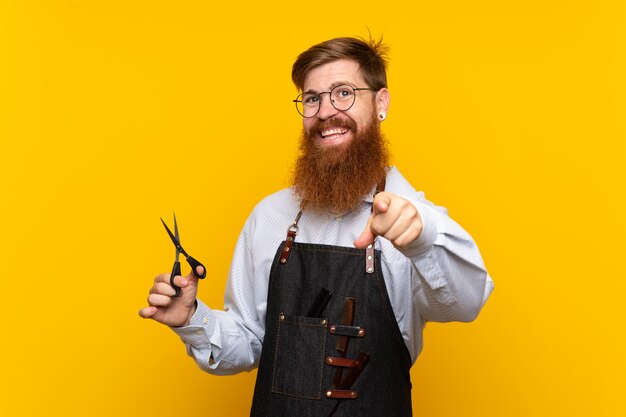 Barber avec une longue barbe dans un tablier pointe le doigt avec une expression confiante