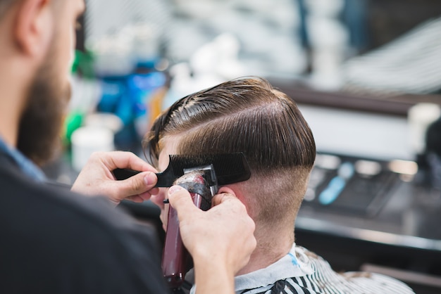 Barbier avec barbe coupe le jeune homme avec une tondeuse à cheveux dans un salon de beauté pour hommes.