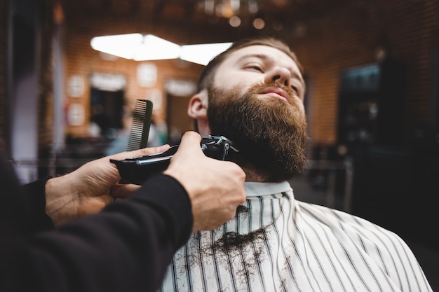 Un barbier coupe la barbe à un gars brutal