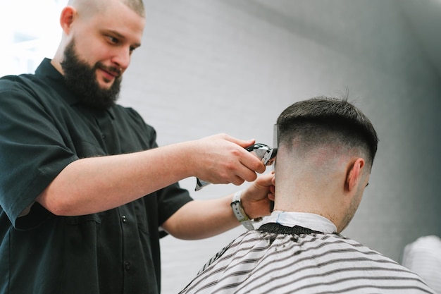 Un barbier joyeux crée une coiffure à la mode pour le client