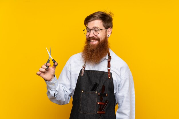 Barbier avec une longue barbe dans un tablier sur un mur jaune isolé avec expression heureuse