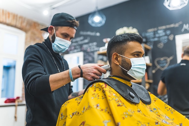 Un barbier professionnel portant un masque coupe les cheveux du cou de son client dans un barbier.