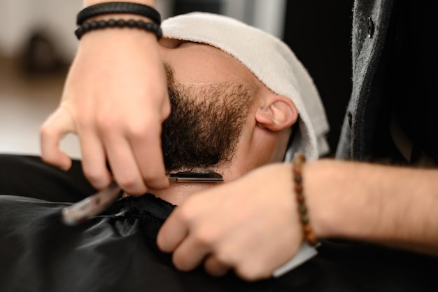 Un barbier rase le cou d'un client barbu avec un rasoir dangereux. Il rase le contour de la barbe pour obtenir la forme correcte.