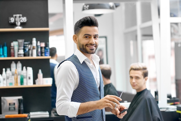 Barbier souriant debout près de jeune cliente assis près du miroir.