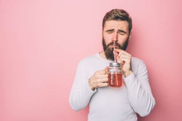 Un barbu dans un pull blanc boit du thé dans la tasse bien que la paille