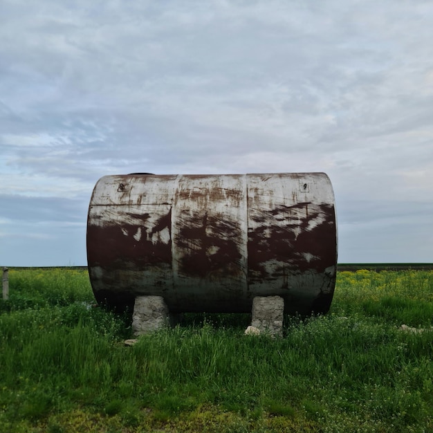 Un baril rouillé se trouve dans un champ d'herbe et de fleurs.