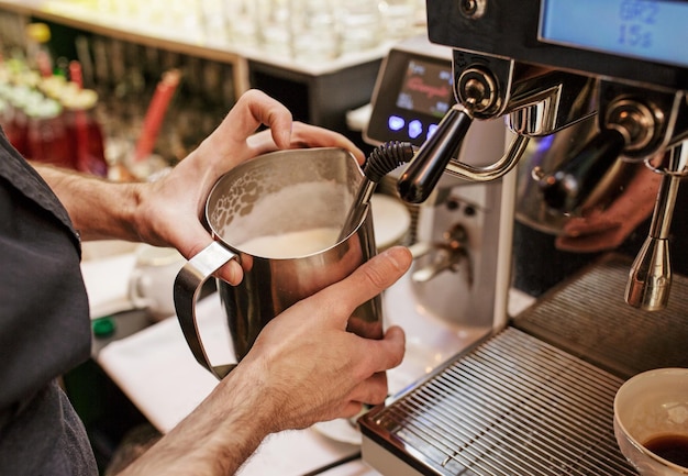 Barista dans un café-bar préparant un cappuccino approprié versant du lait moussé dans une tasse de café faisant la création de modèles d'art latte Concept de restauration de service professionnel