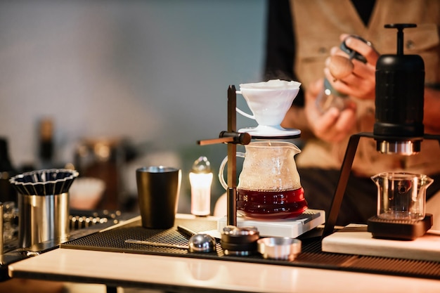 Barista faisant du café au goutte-à-goutte avec de l'eau chaude versée à partir d'une bouilloire Grains de café moulus contenus dans un filtre Faire du café à goutte à goutte Café de bar lent