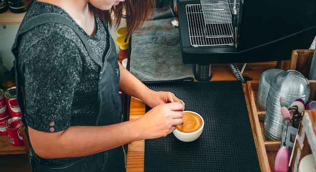 Barista faisant du café avec une cuillère en bois faisant ou préparant de la mousse de café dans une tasse de café